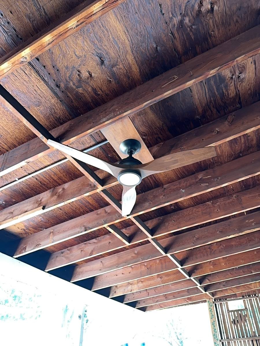 Ceiling fan mounted between exposed wooden beams on a covered patio