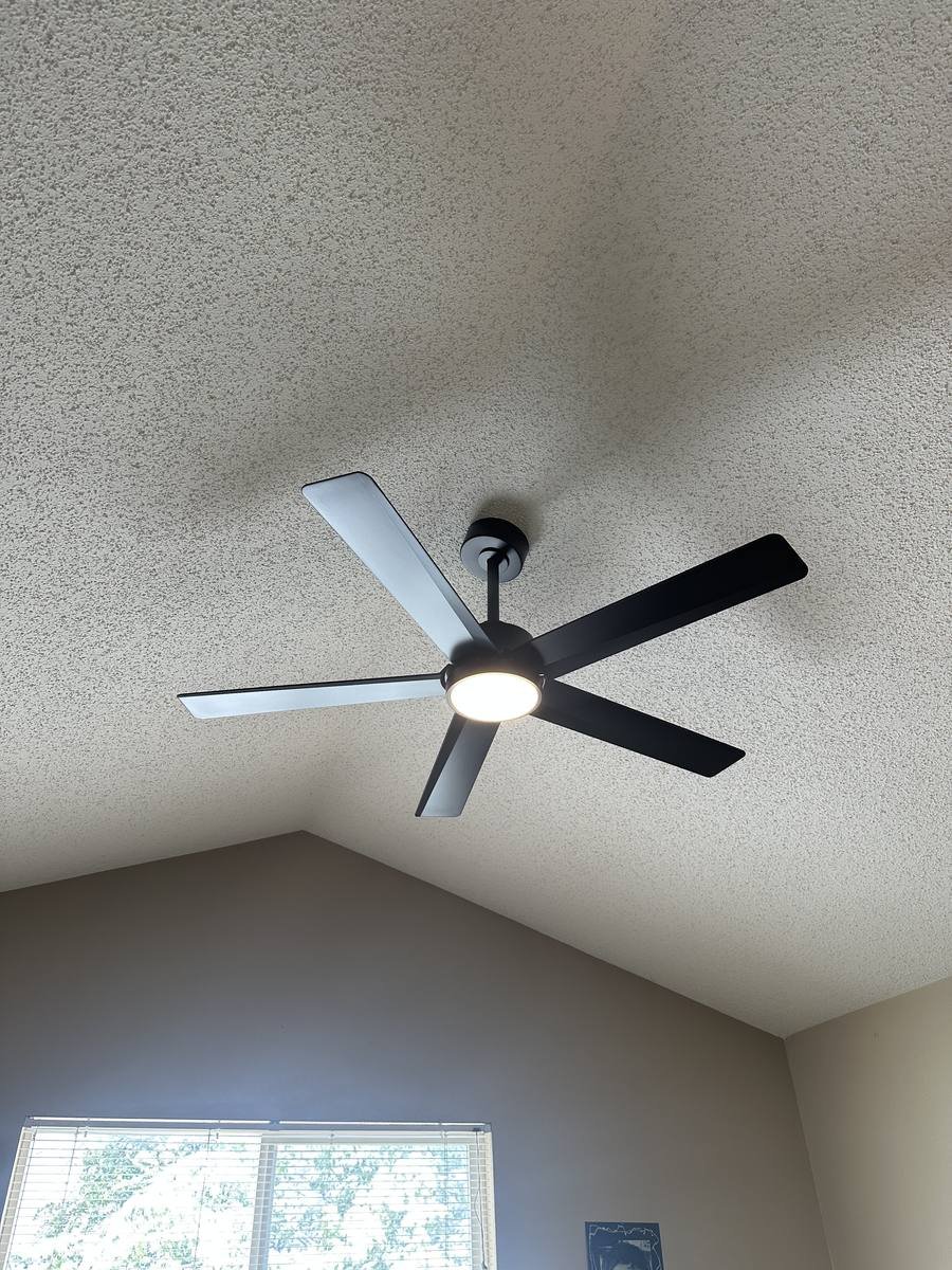 Black five-blade ceiling fan installed on a sloped ceiling with the light on