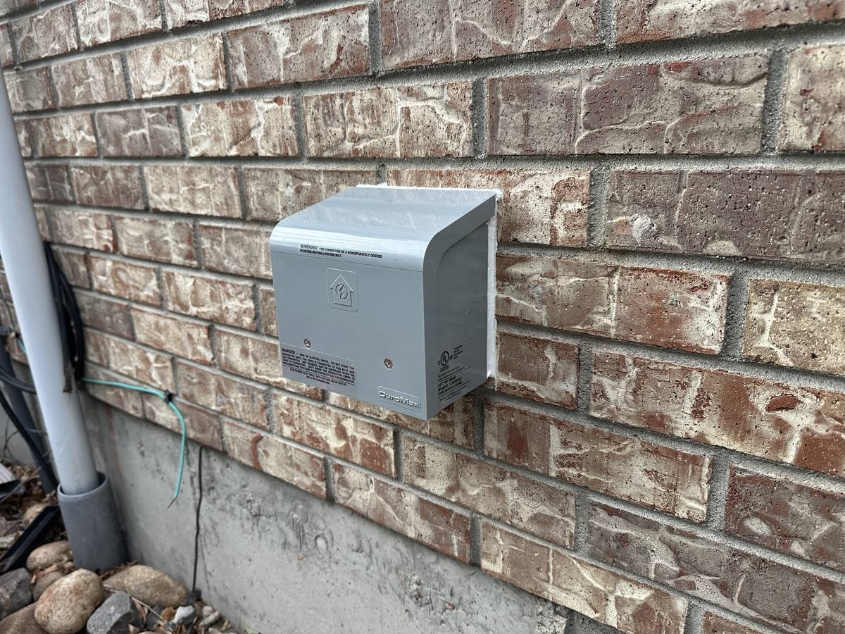 Gray weatherproof generator inlet box mounted on an exterior brick wall