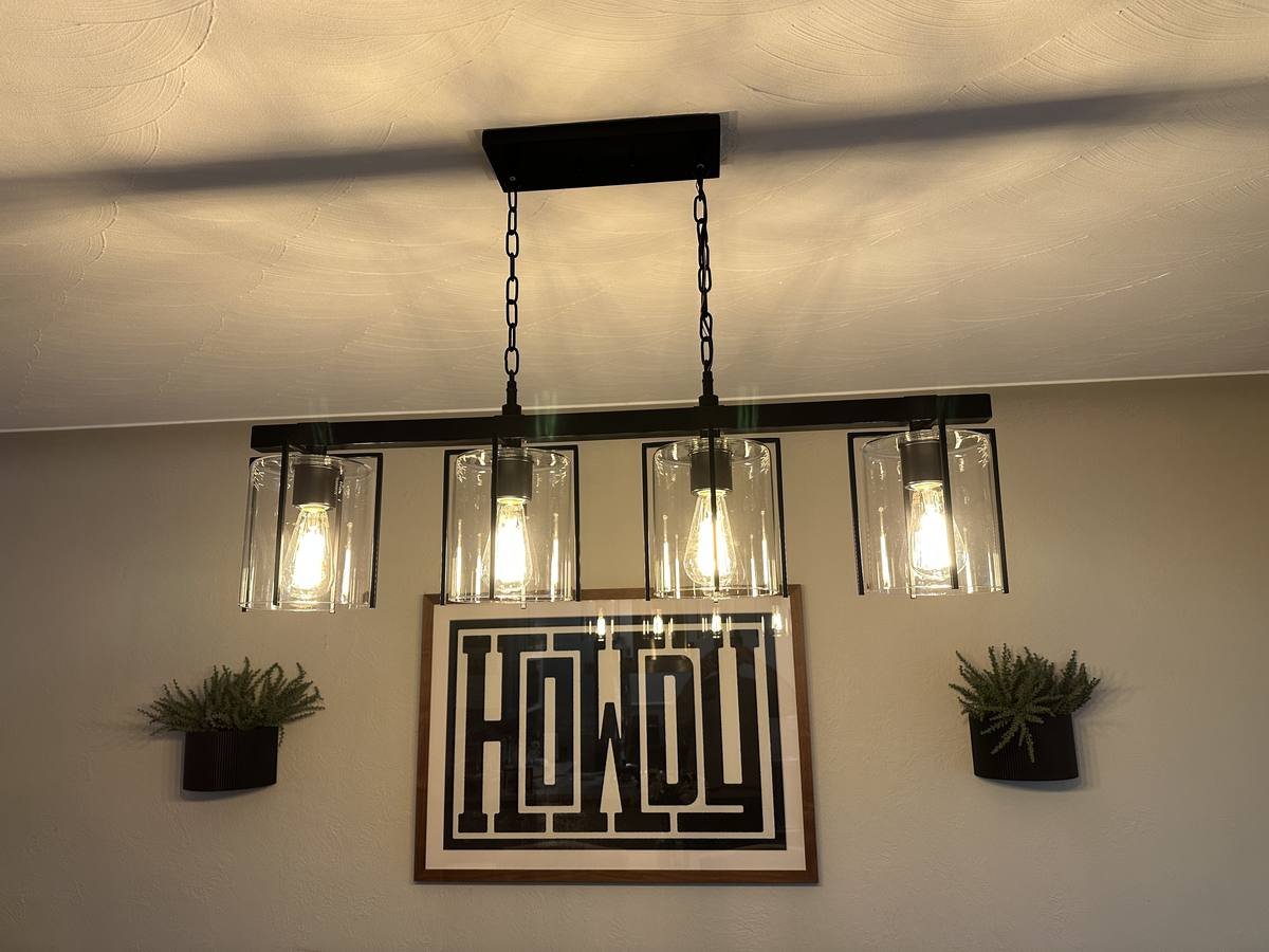 Black linear pendant light with four glass shades hanging over a dining area