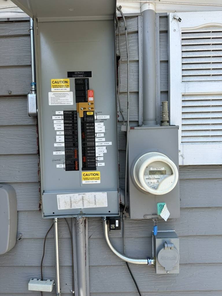Outdoor electrical panel with a generator interlock, every breaker labeled, and caution labels beside the meter
