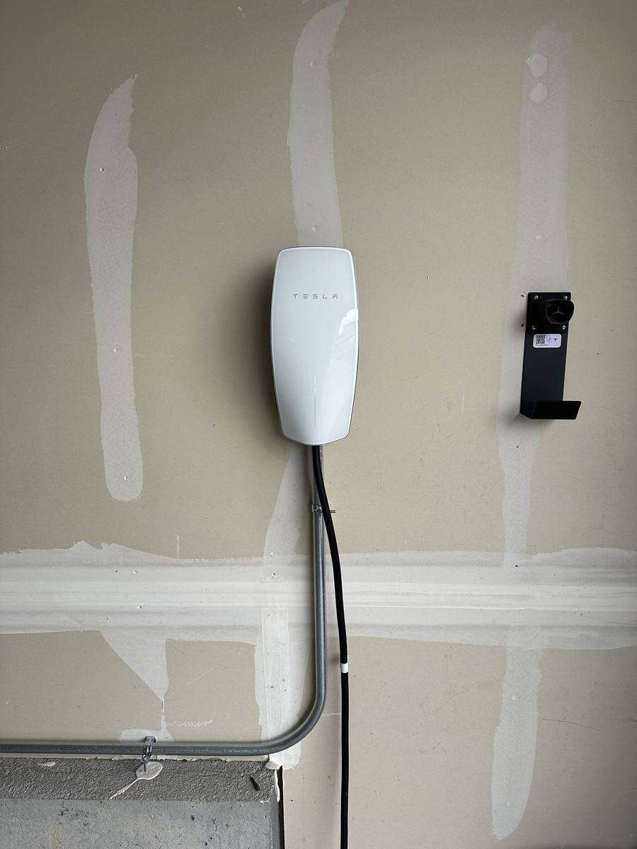 Tesla Wall Connector mounted on a garage wall with metal conduit running to it