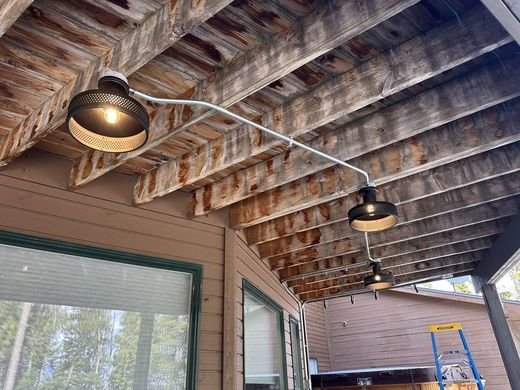 Barn-style pendant lights on exposed conduit under a patio beam